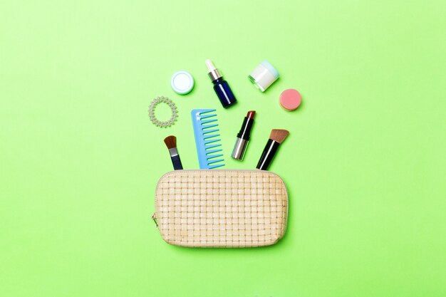 Top view od cosmetics bag with spilled out make up products on green