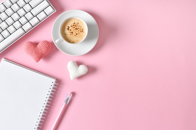 Top view of the office desk Romantic atmosphere A notebook with a cup of coffee hearts and a keyboard on a pink background