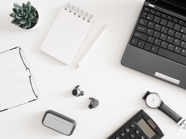 Top view of office desk table with laptop, calculator, pen and notebook on white background