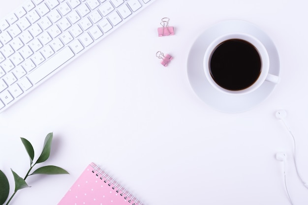 Top view office desk with cup of coffee, keyboard, notebook and stationery.