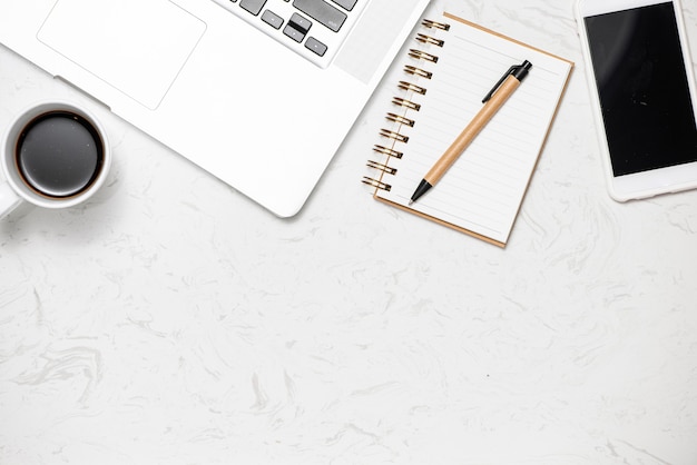 Top view office desk with keyboard, notebooks and coffee cup on marble background.