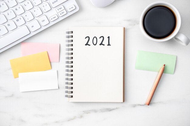 Top view of office table desk 2021 Goal work concept with keyboard, notebook, pencil, eyeglasses and coffee