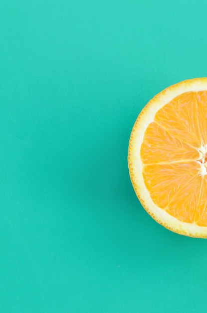 Top view of a one orange fruit slice on bright background in turquoise green color. A saturated citrus texture image