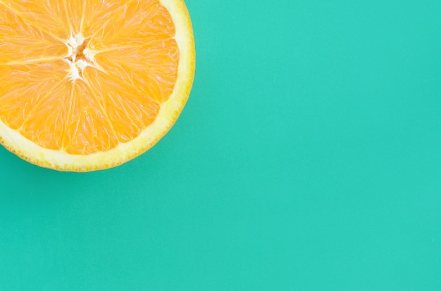 Top view of a one orange fruit slice on bright background in turquoise green color. 