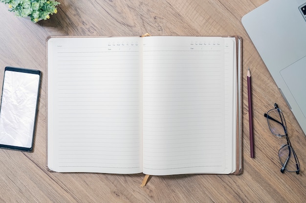 Top view of open blank page notebook with supplies on wooden table.