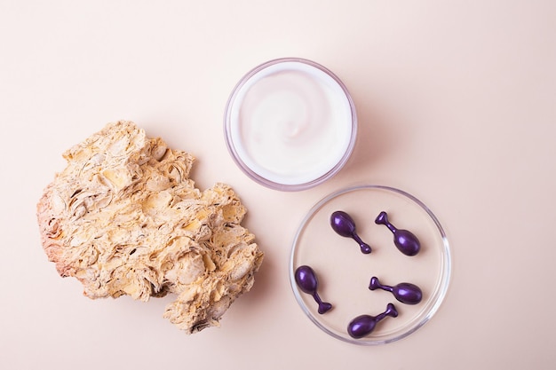 Top view of open box with white cream and cosmetics capsules in petri dish near it