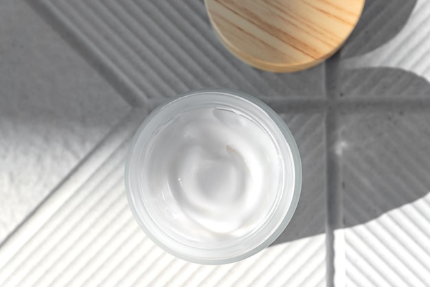 Top view of open glass jar with face cream with peptides for anti aging effect on concrete background Minimalism style