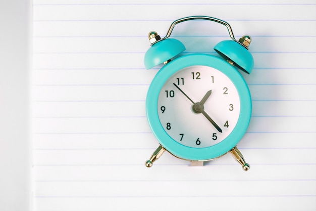 Top view of an open notepad, blue alarm clock.