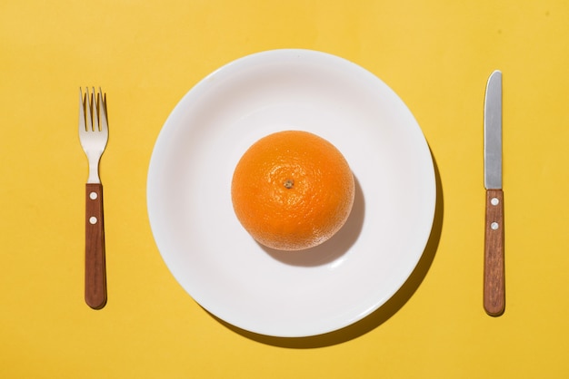 Top view of orange fruit on white plate with knife and fork on yellow background