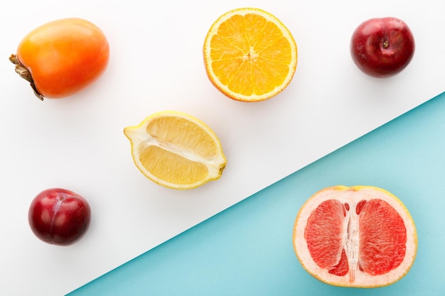 Top view of orange lemon and grapefruit halves with persimmon apples on white and blue background