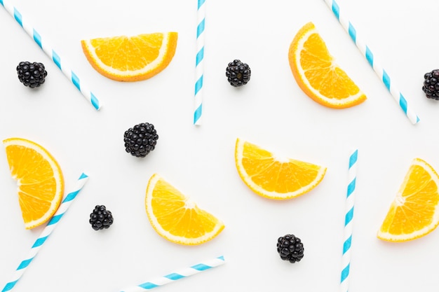 Top view of orange slices and blackberries  with straws for juice