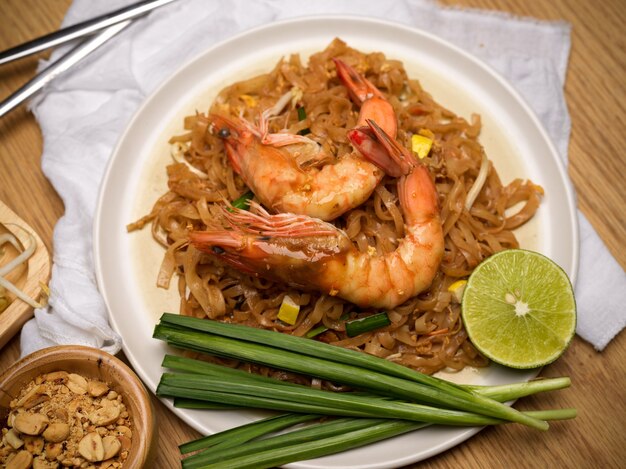 Top view of Pad Thai, stir fired Thai noodles with shrimps serving with lime, beansprouts and chives on dinning table, Thai traditional food