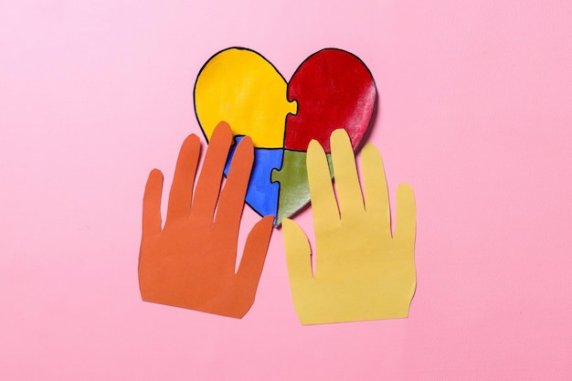 Top view of paper hands shape on colorful puzzle heart World Autism Awareness Day or month concept