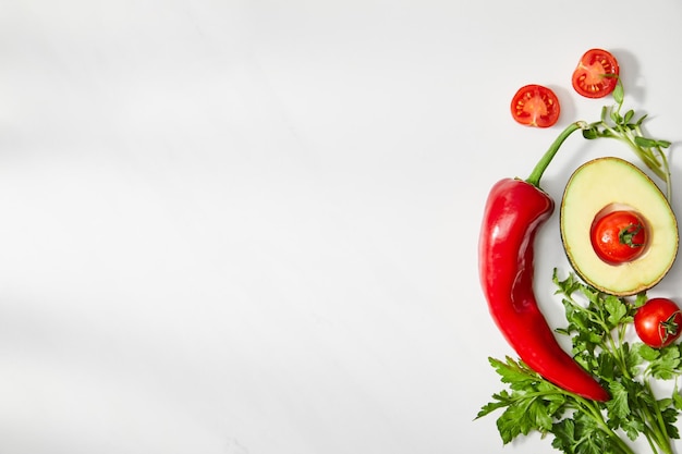 Top view of parsley chili pepper cherry tomatoes and avocado half on white background