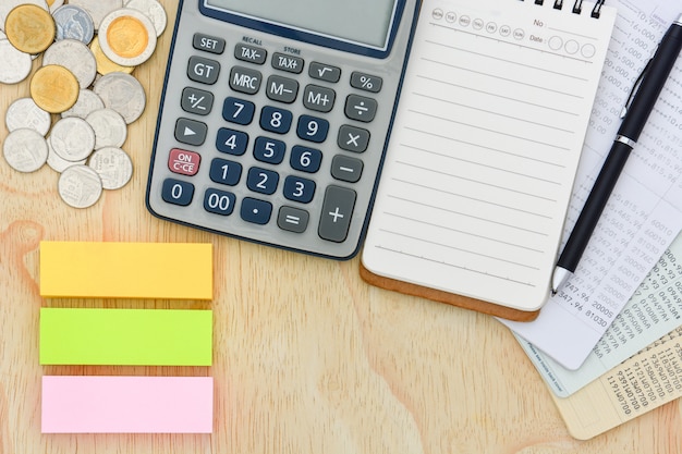 Top view of passbooks saving account, calculator, notebook and pile of coins on wood background