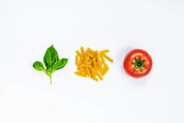 Top view of pasta ingredients on white background - raw fusilli, fresh basil and ripe tomatoe. Italian food concept.