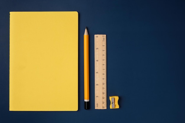 Top view pastel yellow notebook with yellow pencil and notepad on navy blue working table