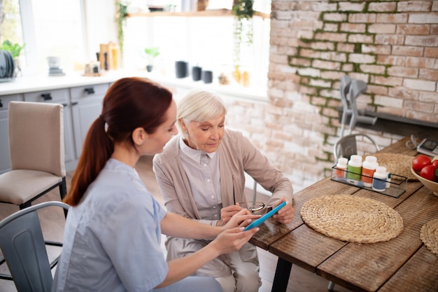 Top view of pensioner using tablet with help of caregiver