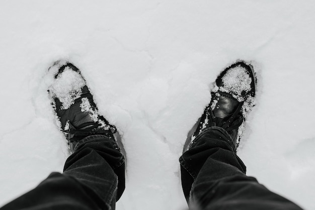 Top view person in black leather boots standing in snowdrift on winter day outdoors closeup