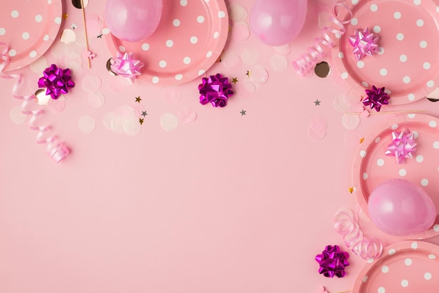 Top view photo of birthday composition with pink and violet ribbon stars serpentine paper plates balloons and confetti on isolated pastel pink background with copyspace