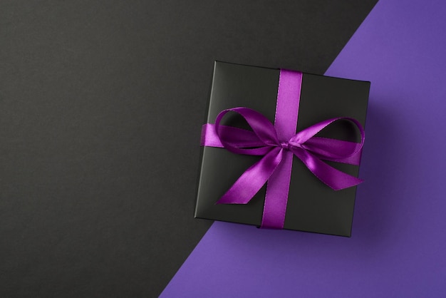 Top view photo of black giftbox with purple ribbon bow on isolated bicolor violet and black background with copyspace