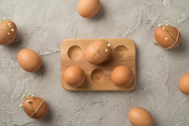 Top view photo of brown easter eggs decorated by gypsophila flowers and twine in wooden egg holder on isolated grey concrete background