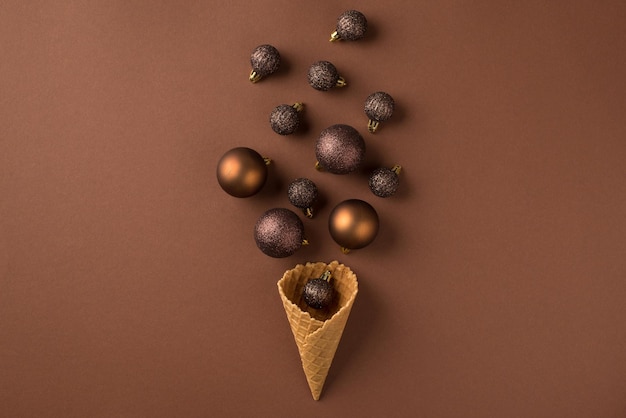 Photo top view photo of brown and gold christmas tree balls flying out of ice cream cone on isolated brown background