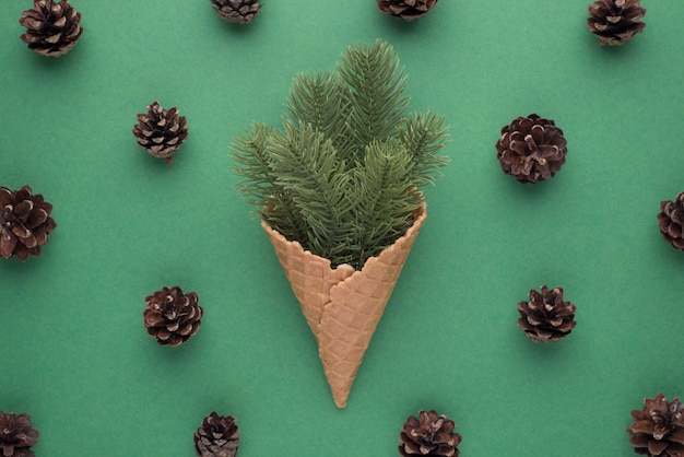 Top view photo of christmas decorations ice cream cone with pine twigs and pine cones on isolated green background