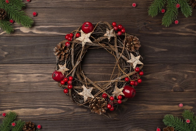 Top view photo of christmas decorations pine branches and twig wreath with holly berries and pine cones on isolated dark wooden desk background