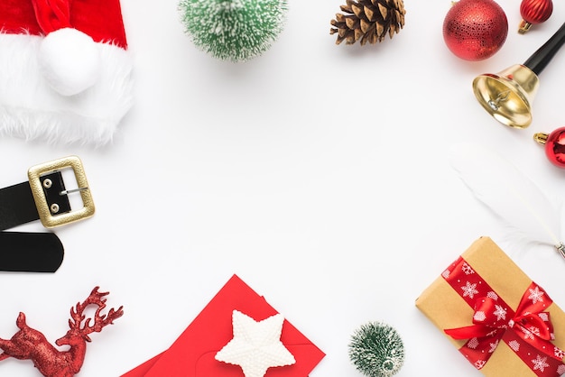 Top view photo of christmas decorations santa claus hat belt red balls reindeer pine toys envelopes star giftbox quill bell and pine cone on isolated white background with copyspace in the middle