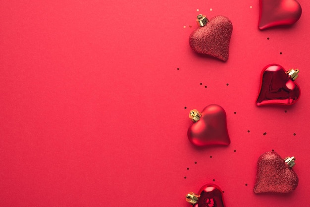 Top view photo of christmas tree decorations red heartshaped balls and sequins on isolated red background with copyspace