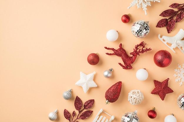 Top view photo of composition white silver and red christmas tree decorations snowflakes stars disco balls cone deer small ice skates sleigh and sprigs on isolated beige background with copyspace