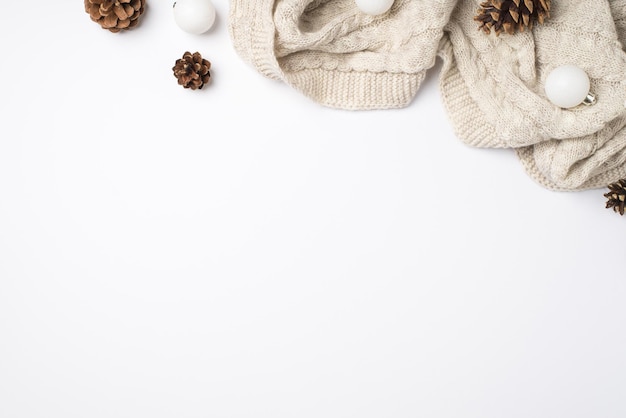 Top view photo of cozy knitted scarf pine cones and white christmas tree balls on isolated white background with empty space