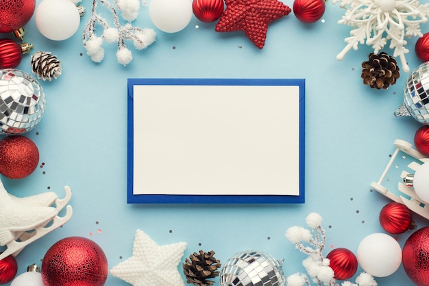 Top view photo of envelope paper sheet white and red christmas tree decorations snowy twigs pine cones and sequins on isolated pastel blue background with blank space