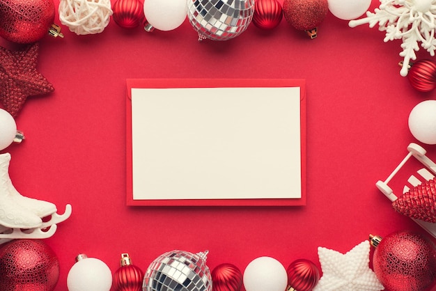 Top view photo of envelope with card white and red christmas tree decorations disco balls stars snowflake small sleigh and ice skates on isolated red background with copyspace