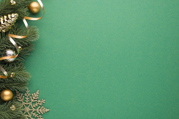 Top view photo of gold and silver christmas tree balls toy cone small bells snowflake and serpentine on pine twigs on isolated green background with blank space