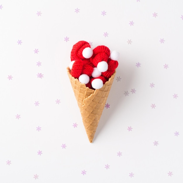 Top view photo of ice cream cone with small bobble hats and confetti on isolated white background