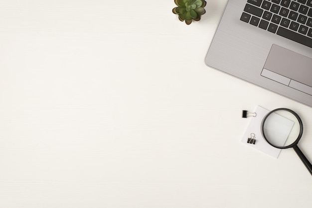 Top view photo of laptop magnifier binder clips sticker note and flowerpot on isolated white wooden table background with copyspace