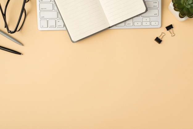 Top view photo of open grey reminder on white keyboard plant glasses pens and binders on isolated beige background with copyspace