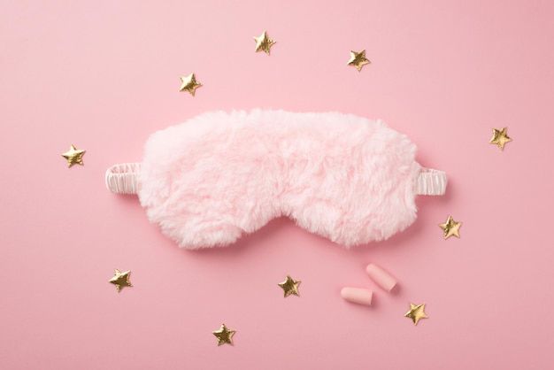 Top view photo of pink fluffy sleeping mask earplugs and golden stars on isolated pastel pink background with copyspace