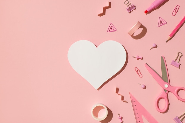 Top view photo of pink stationery adhesive tapes pins binder clips scissors pencil felt pen ruler and white paper heart on isolated light pink background with copyspace