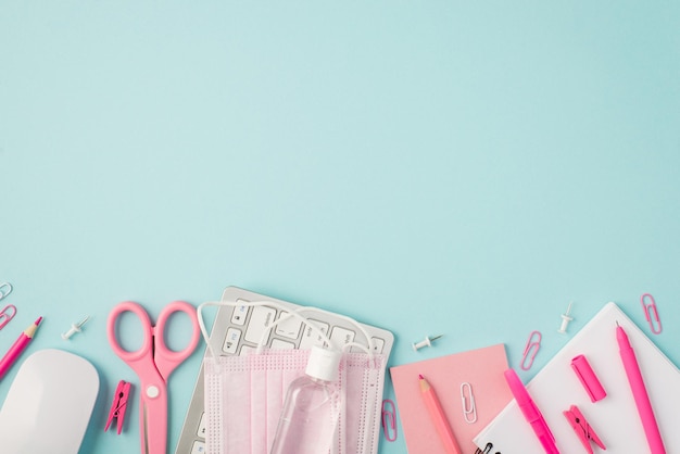 Top view photo of pink stationery pens pencils scissors pins clips sticker reminder keyboard mouse sanitizer medical facemasks on isolated pastel blue background with copyspace