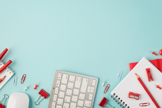 Top view photo of red stationery pens pencils binders pins clips sharpener notebooks keyboard and mouse on isolated pastel blue background with copyspace