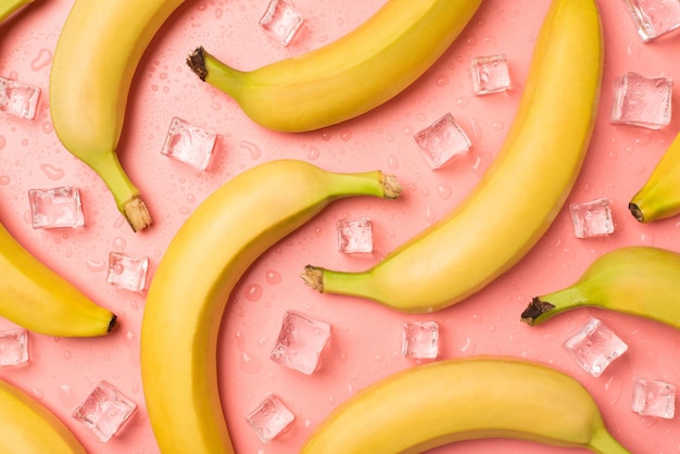 Top view photo of ripe unpeeled bananas ice cubes and drops on isolated light pink background