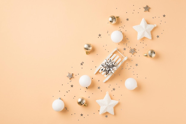 Top view photo of row composition white and golden christmas tree decorations small sleigh with silver star balls stars and sequins on isolated beige background with copyspace