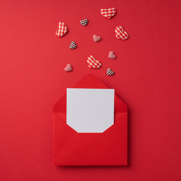 Top view photo of st valentine's day decorations open red envelope with paper card and checkered hearts on isolated red background with blank space