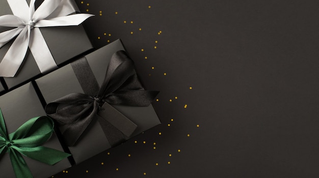 Top view photo of three black gift boxes with black white and green ribbon bows and golden sequins on isolated black background with copyspace