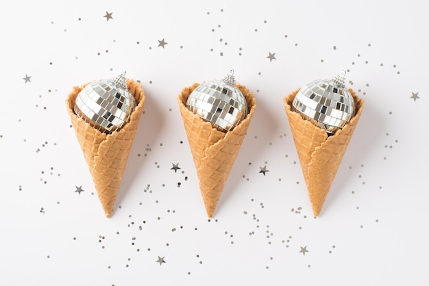 Top view photo of three ice cream cones with christmas tree disco balls and silver confetti on isolated white background