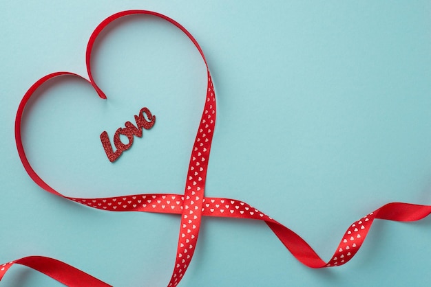 Photo top view photo of valentine's day decorations inscription love in red silk ribbon heart on isolated pastel blue background with blank space