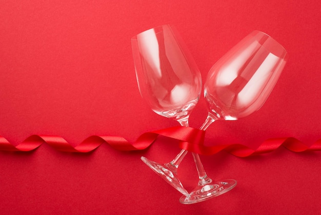 Top view photo of valentine's day decorations red curly ribbon and two wineglasses on isolated red background with copyspace